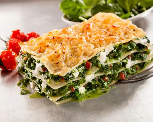 Deliciosa lasaña de verduras, con capas de pasta, espinacas y queso cremoso, acompañada de tomates cherry.