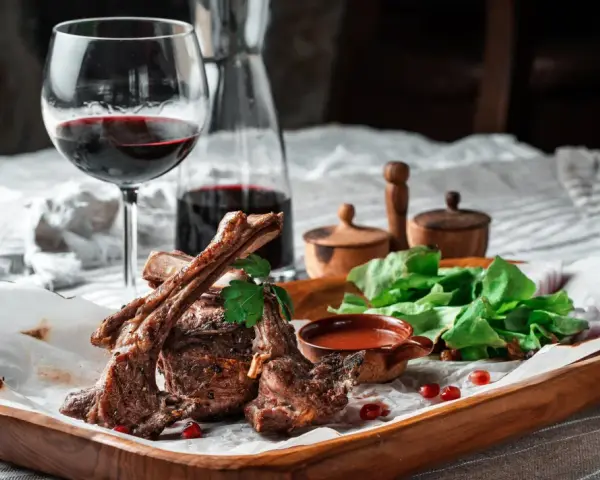 Saftige Lammkoteletts mit frischem Salat und einem Glas Rotwein. Die perfekte Wahl, welcher Wein zu Lamm passt, ist oft ein kräftiger Rotwein.