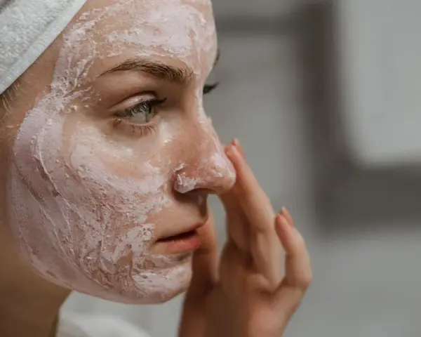 Mujer con mascarilla rosa en la cara, aprendiendo como exfoliar la cara para una piel radiante.