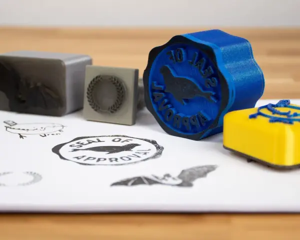 A blue 3d print stamp with a seal of approval design sits next to a yellow one.
