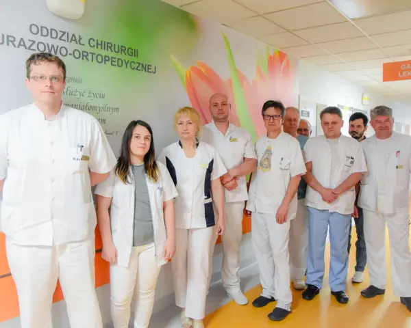 Grupa lekarzy w białych fartuchach stoi w szpitalnym korytarzu.