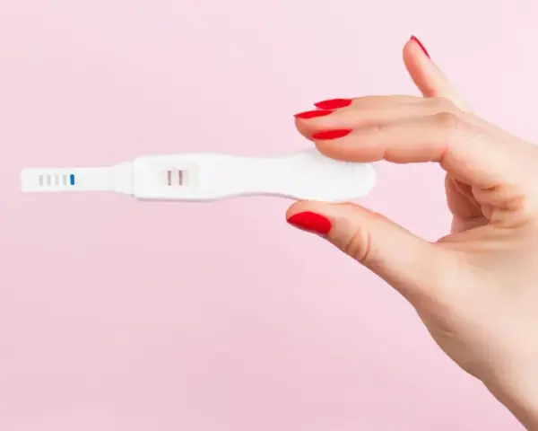 Dłoń z czerwonymi paznokciami trzyma test ciążowy z dwoma kreskami. To może być sygnał, że doszło do ciąży biochemicznej.