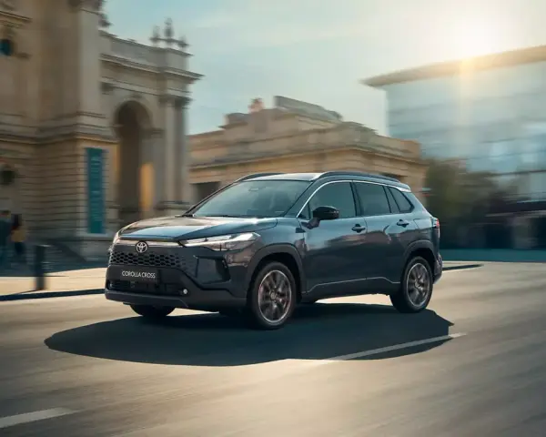 Ciemnoszary Toyota Corolla Cross sunie ulicą miasta, mijając zabytkowe budynki i nowoczesne szklane fasady.