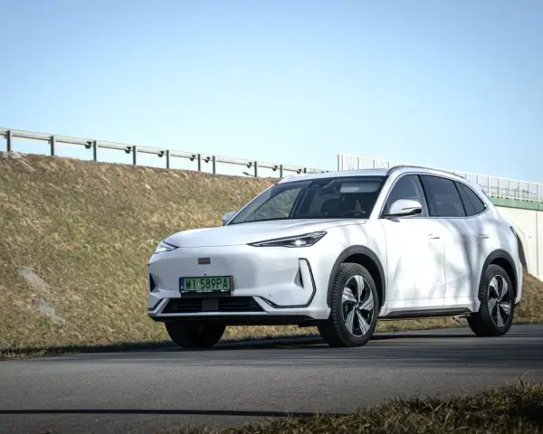 Biały SUV Geely E5 (EX5) na tle wiaduktu i niebieskiego nieba.