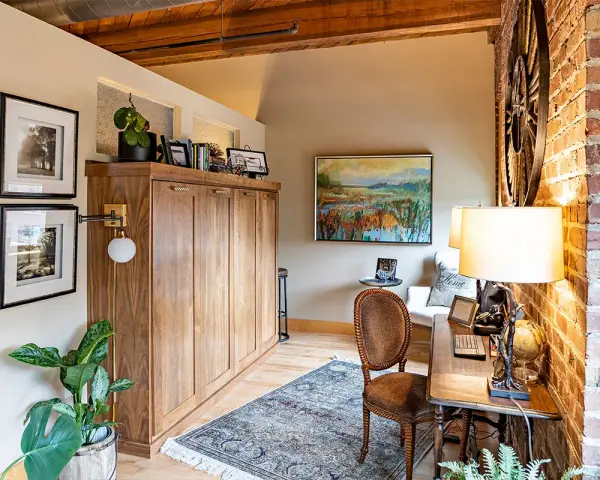 Accogliente angolo studio con un armadio a scomparsa in legno, un tappeto persiano e un quadro paesaggistico, che evoca l'atmosfera di una piccola casa di campagna.