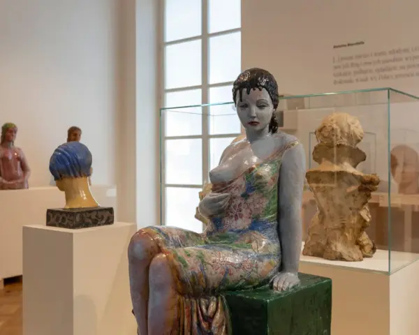 Ceramiczna rzeźba kobiety w kwiecistej sukni, dzieło inspirowane twórczością Olgi Niewskiej, prezentowana w muzeum.