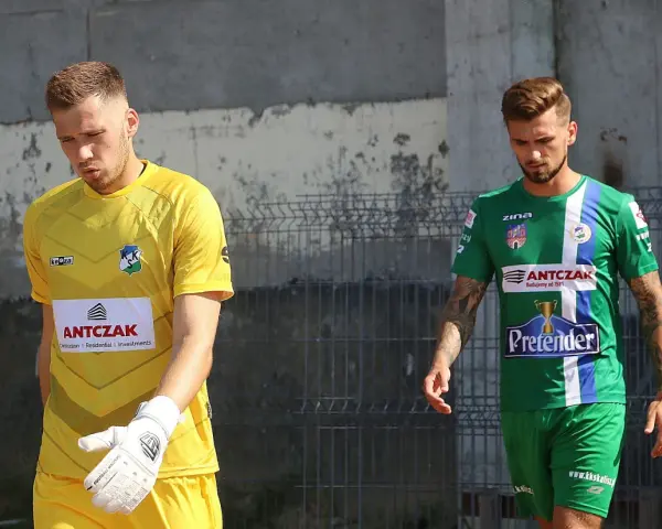 Dwóch piłkarzy, w tym Michał Kaszuba w żółtej koszulce bramkarza, idzie obok siebie.