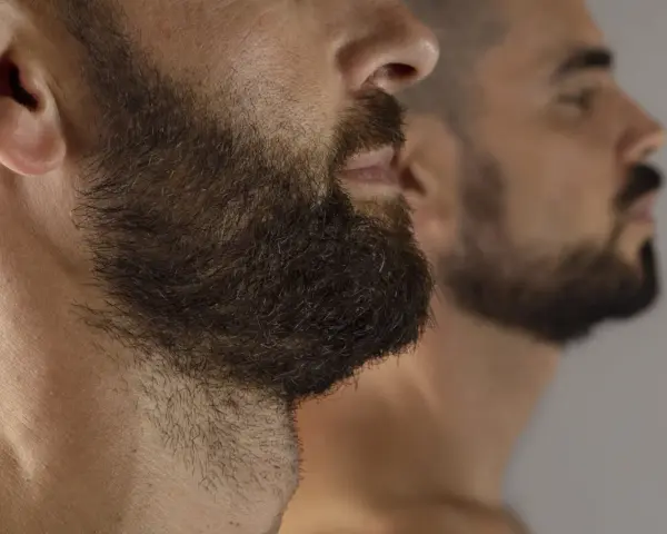 Primer plano de un hombre con barba oscura y tupida, reflejado en un espejo. La imagen captura la decisión de dejar crecer la barba.