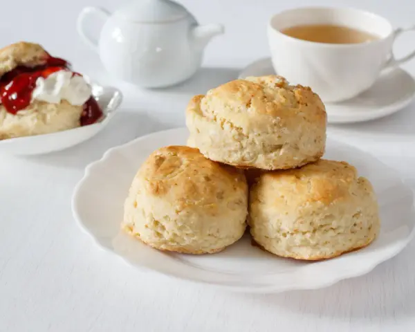 Goldbraune Scones, ein Klassiker zum Tee. Sie sind kleine, süße Gebäckstücke, die oft mit Marmelade und Sahne serviert werden.