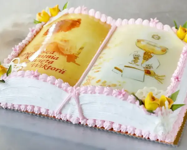 Eleganckie ciasto na komunię w kształcie otwartej księgi z motywami religijnymi i napisem "Pierwsza Komunia Święta Wiktorii".