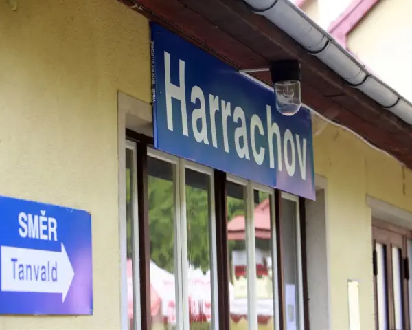 Tabliczka "Harrachov" nad oknami dworca. Obok znak kierunkowy "Směr Tanvald". Pociąg Szklarska Poręba Harrachov czeka na pasażerów.