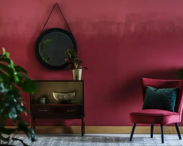 Eleganckie wnętrze w odcieniu **kolor burgundowy**. Aksamitny fotel, lustro i stylowa komoda tworzą przytulną atmosferę.