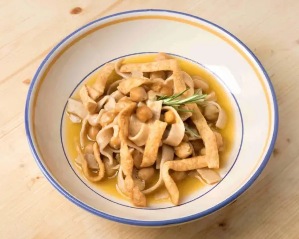 Un piatto di ciceri e tria, pasta fresca con ceci e sfoglie fritte, guarnito con rosmarino.