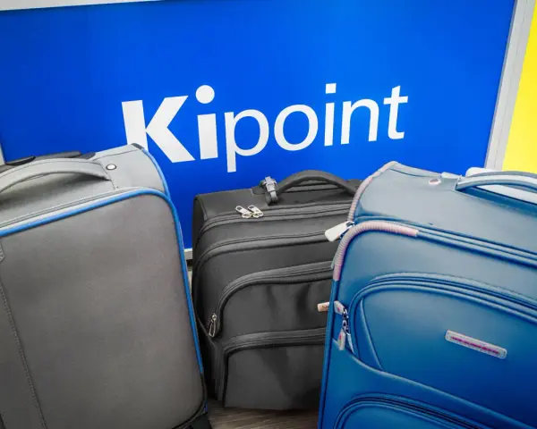 Three suitcases in front of a blue sign with "Kipoint" in white letters.