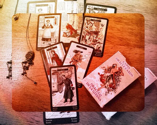 Rozłożone karty cygańskie, w tym "Służąca", "Żołnierz" i "Nieszczęście", obok pudełka "Gypsy Oracle Cards".