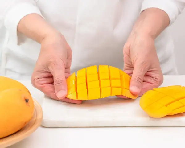 Ręce kroją dojrzałe mango na kostki. Czy mango ma pestkę? Tak, ale jej nie widać, bo jest w środku.