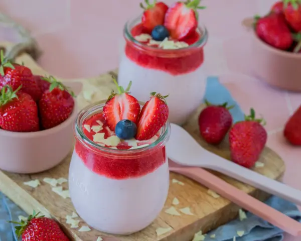 Zwei Gläser mit cremigem Joghurt und Erdbeersoße, garniert mit frischen Erdbeeren und Blaubeeren. Ein schneller Nachtisch mit Erdbeeren, der Lust auf mehr macht.