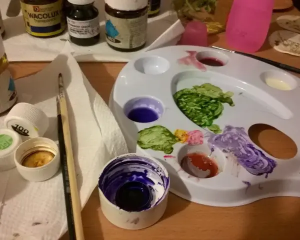 Paleta z farbami i pędzel, idealne do malowania gliny samoutwardzalnej. Kolory na palecie to zielony, fioletowy, czerwony i żółty.