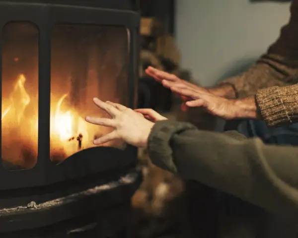 Manos calentándose frente a una chimenea con llamas danzantes. Los tubos de aire de la chimenea ayudan a distribuir el calor.