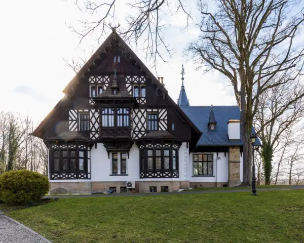 Pałac myśliwski w Promnicach, z charakterystyczną architekturą szachulcową i zdobieniami, otoczony drzewami.