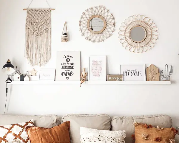 Idee per arredare parete dietro divano: macramè, specchi, quadri con scritte e oggetti decorativi creano un angolo accogliente.