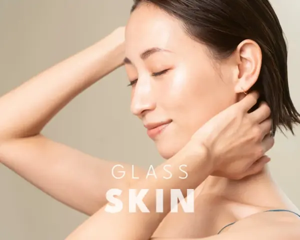 Kobieta z idealną, lśniącą cerą typu "glass skin", z dłońmi przy szyi i ramieniu.