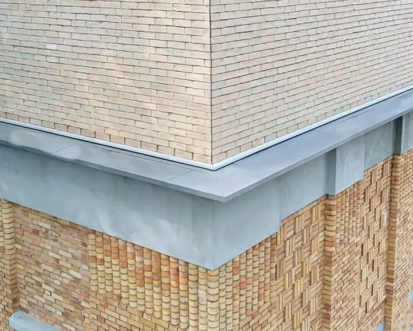 Narożnik budynku z ceglaną elewacją i nowoczesną attyką. Detale architektoniczne podkreślają fakturę muru.