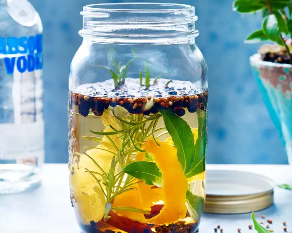 Ein Glas mit Zutaten für ein Sloe Gin Rezept: Wacholder, Zimt, Zitronenschale, Rosmarin und Lorbeerblätter in Alkohol.