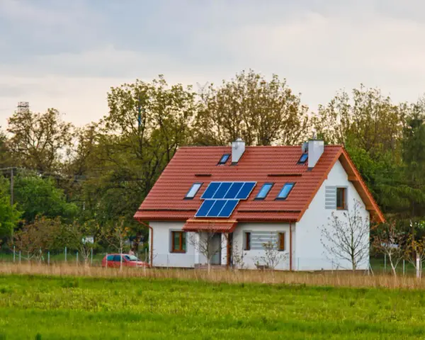 Nowoczesny dom energooszczędny z panelami słonecznymi na dachu, otoczony zielenią.