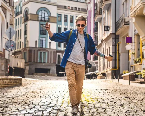 Giovane con caffè e smartphone cammina in città su un selciato, godendosi la musica e il paesaggio urbano.