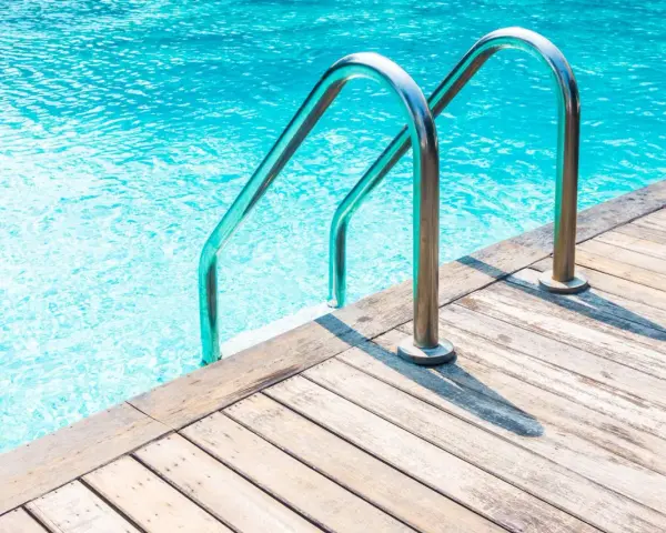 Escalera de piscina de obra con barandillas cromadas sobre tarima de madera. ¿Cuánto cuesta una piscina de obra?