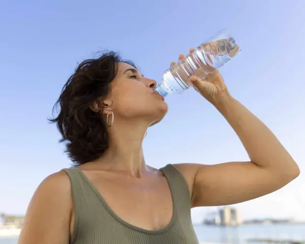 Donna beve acqua per combattere il caldo e la depressione, con il cielo azzurro sullo sfondo.