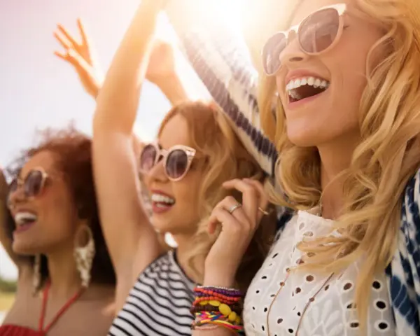 Trois amies profitent d'un festival ensoleillé, leurs rires atteignant un niveau sonore équivalent à 66 décibels.