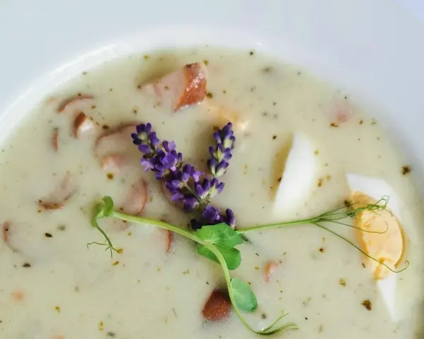 Aromaticzny żurek z kiełbasą i jajkiem, ozdobiony gałązką lawendy i kiełkami.