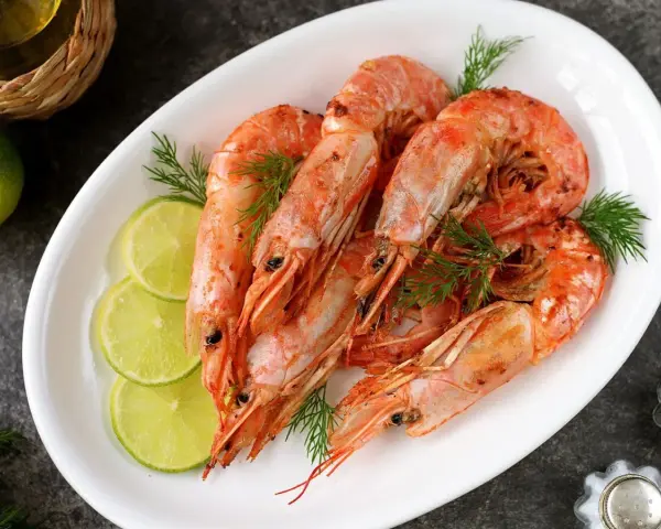 Plato blanco con langostinos cocidos, rodajas de limón y eneldo. Ideal para recetas con langostinos.