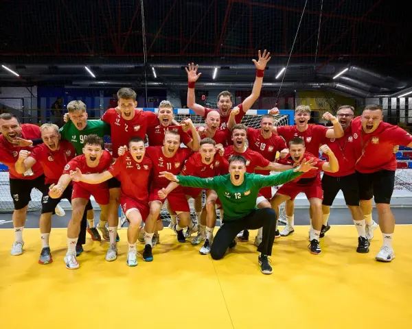 Drużyna piłkarzy ręcznych w czerwonych strojach świętuje zwycięstwo. Wśród nich Krzysztof Zimny, bramkarz w zielonym stroju, klęczy z wyciągniętymi rękami.