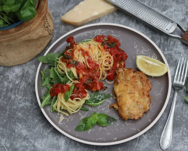 Piccata Milanese: goldbraunes Schnitzel mit Spaghetti in Tomatensauce, garniert mit Rucola und Zitrone.
