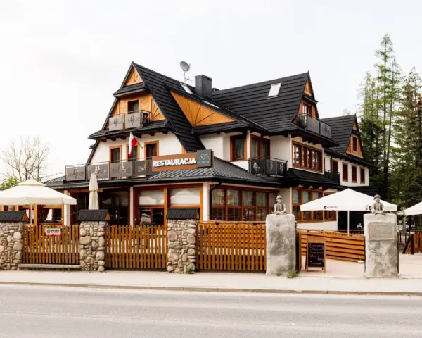 Szukasz miejsca, gdzie zjeść w Kościelisku? Ta restauracja z drewnianym ogrodzeniem i białymi parasolami zaprasza na góralskie smaki.