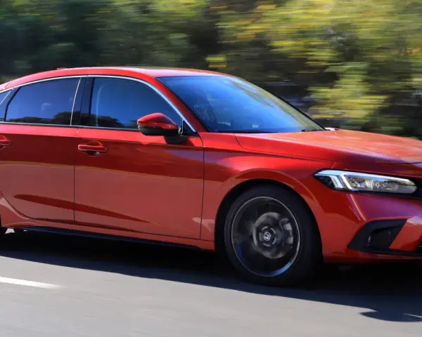 Czerwony Honda Civic 11. generacji pędzi po drodze, otoczony zielenią drzew.