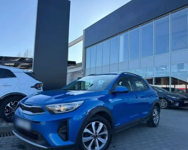 Błękitny Kia Stonic 2023 zaparkowany przed salonem samochodowym. Obok stoi biały SUV.