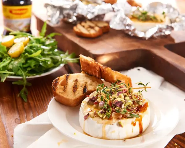 Pyszny camembert z grilla, polany miodem i posypany pistacjami, podany z grzankami i sałatką. Idealny na letnie wieczory.