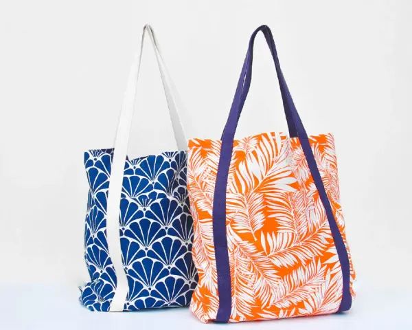 Deux sacs fourre-tout aux motifs vibrants : un bleu avec des éventails blancs, l'autre orange avec des feuilles de palmier blanches. Un patron de sac gratuit à télécharger pour créer vos propres accessoires.