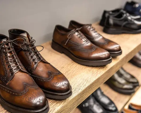 Scarpe marchigiane famose: eleganti stivaletti e stringate in cuoio marrone, con dettagli traforati, su uno scaffale di legno.