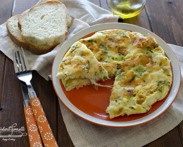 Una soffice frittata di albumi con erbe aromatiche, servita su un piatto arancione, accanto a fette di pane tostato e una forchetta.