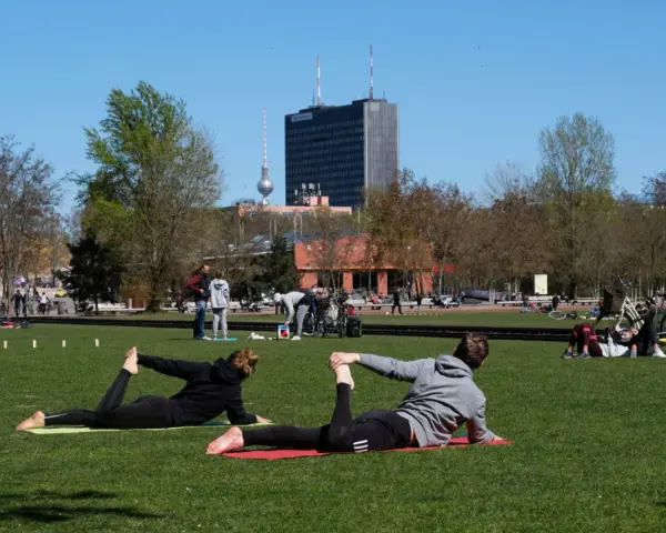 Menschen machen Yoga und entspannen sich im Park. Ein sonniger Tag für Sport in Berlin mit dem Fernsehturm im Hintergrund.