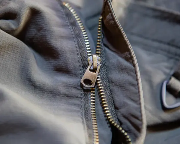 Detalle de una cremallera de chaqueta que se ha salido, mostrando el cursor metálico y los dientes.