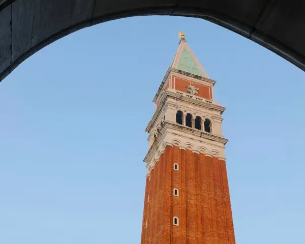 Vista dal campanile di San Marco: la torre in mattoni rossi si staglia contro il cielo azzurro, incorniciata da un arco di pietra.