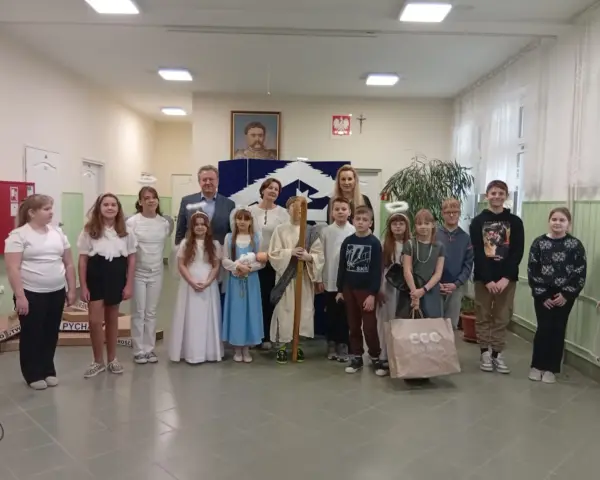 Dzieci w strojach aniołów i pasterzy, odgrywające baśń o dobrym synku. W tle portret i dekoracje.