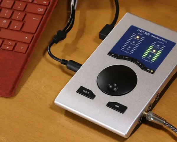 Srebrny interfejs audio RME Babyface Pro FS podłączony do czerwonej klawiatury. Idealny do mobilnego studia.