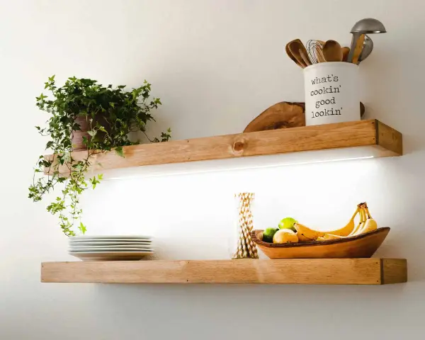 Estantes de madera con iluminación LED oculta, ideal para saber como colocar tiras led en estantes. Exhiben plantas, vajilla y frutas.